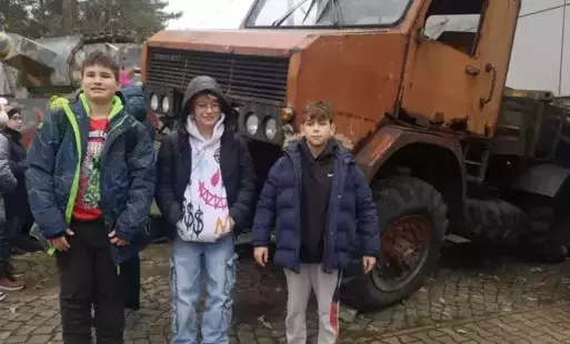 Trzech chłopców z klasy 5 stoi na tle starej ciężarówki.