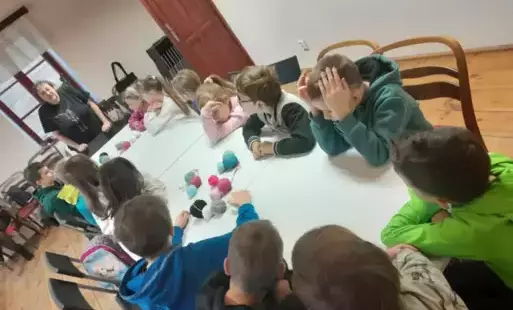 Uczniowie siedzą przy stole, na którym leżą włóczki. 