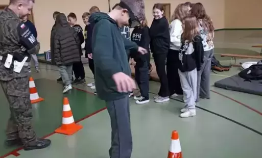 Uczeń pokonuje tor przeszkód z googlami, w tle inni uczniowie oraz przedstawiciel żandarmerii.