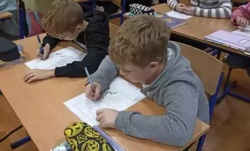 Uczniowie siedzą w ławkach i rozwiązują karty pracy. 