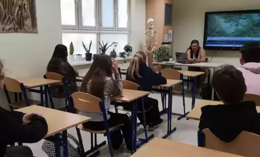 Uczniowie klasy 7A siedzą w ławkach, przy biurku siedzi zaproszony gość