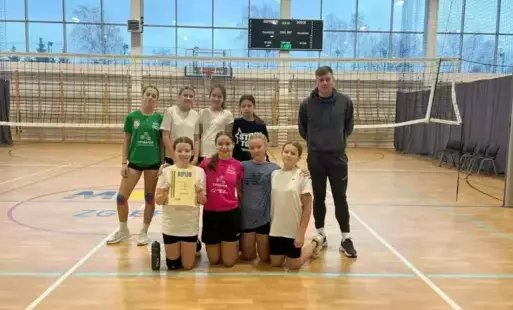 Drużyna siatkarek pozuje na boisku z nauczycielem wychowania fizycznego 