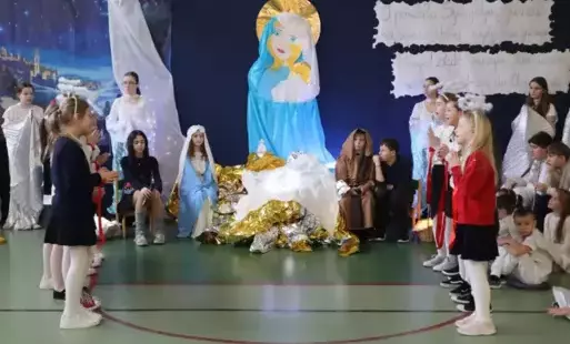 Uczniowie na tle świątecznej dekoracji, po środku aktorzy grający Maryję i Józefa, wokół dzieci. 