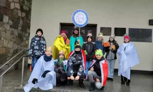 Uczniowie szkoły na schodach kościoła, przebrani w stroje królewskie, z logo szkoły. 