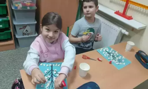 Dwoje uczniów przy ławce robią pracę plastyczną z użyciem popcornu
