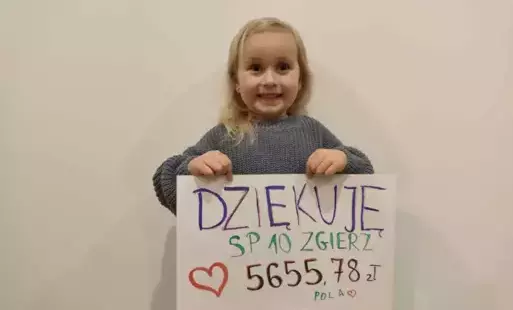Dziewczynka trzyma plakat z podziękowaniem, nazwą szkoły i zebraną kwotą.