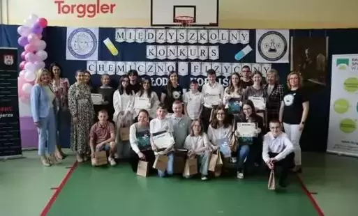 Uczestnicy konkursu z dyplomami stoją na tle dekoracji wraz z dyrekcją szkoły, panią naczelnik i pozostałymi nauczycielami, 