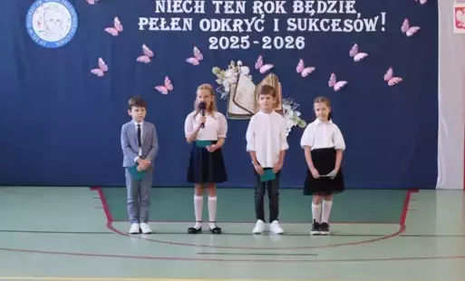 Czworo uczniów klas młodszych ubranych na galowo stoi przed dekoracją 