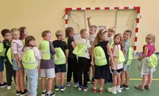 Uczniowie stoją tyłem i pokazują odblaskowe plecaki-worki