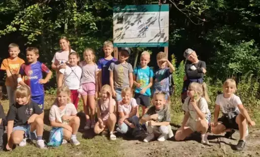 klasa 2b pozuje na tle drzew i tablicy informacyjnej 