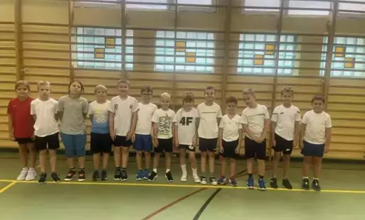 uczniowie klas 1-3 pozują w strojach sportowych na tle drabinek w sali gimnastycznej 