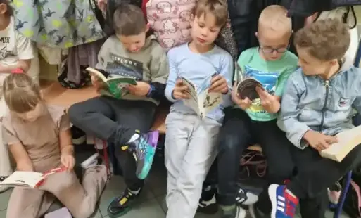 Kilkoro uczniów klasy 2 siedzi na ławce i czyta książki 