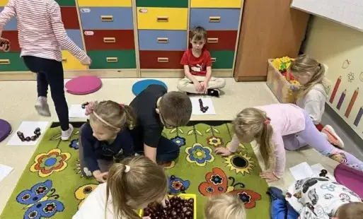 Dzieci w oddziale przedszkolnym na dywanie z kasztanami 