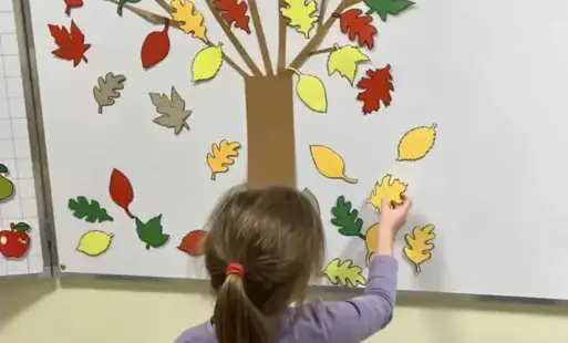 Uczennica przyczepia do drzewa na tablicy kolorowe liście 
