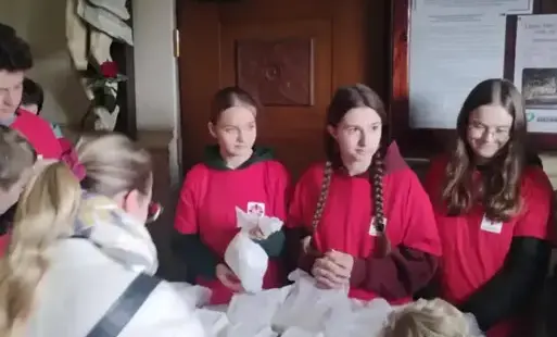 Uczniowie w czerwonych koszulkach z logo Caritasu sprzedają kremówki 