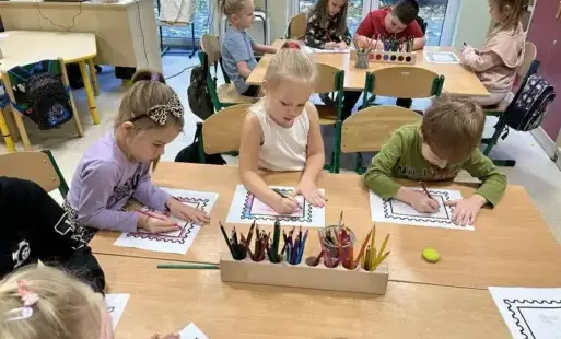 Uczniowie oddziału przedszkolnego przy stolikach kolorują wielkie znaczki pocztowe