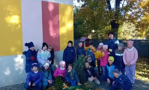 Uczniowie klasy 2B z wychowawczynią pozują na zewnątrz przy szkolnym ogródku 