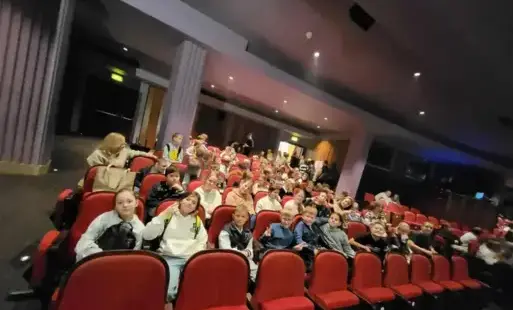 uczniowie siedzą w fotelach na sali teatralnej