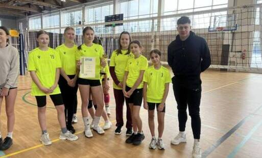 uczennice w jaskrawożółtych koszulkach pozują wraz z nauczycielem na sali sportowej, trzymają dyplom i puchar