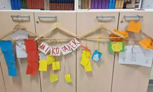 Wiszące na szafkach cztery wieszaki z kolorowymi kartkami. 