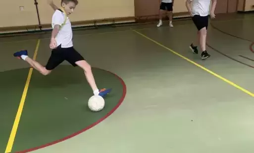 trzech uczniów gra w piłkę nożną, jeden kopie piłkę